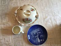 Top view of Bunnykins warming plate with lid, cup, and Copenhagen blue and white porcelain plate laid out on tablecloth