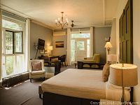 Interior view of guest suite at Frontenac Club Inn showing king bed, seating area, desk, lamps, windows and entry door.