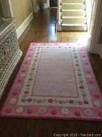 Full view of pink floral border rug laid on hardwood floor in hallway.