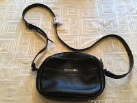 Full view of the black pebbled leather Halston shoulder bag laid flat showing adjustable strap and shape.