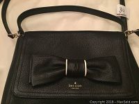 Front view of black pebbled leather handbag showing bow detail and Kate Spade logo