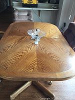 Top-down view of rectangular wooden dining table with parquet-style wood grain top and visible wear.
