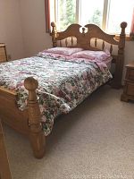 Full view of the wooden double bed with floral bedding and pillows.