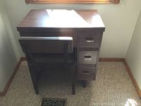 Full view of the wooden sewing table with attached drawers and a matching wooden chair with dark padded seating.