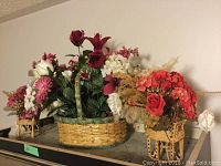 Photo shows three flower baskets: a larger round woven basket with mixed artificial flowers, and two smaller woven baskets with stands filled with dried flowers and grasses.