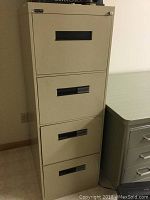 Beige 4-drawer filing cabinet against wall next to a white desk.