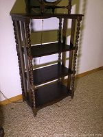 Photo showing antique oak stand against wall with carpeted floor. The stand has four shelves and four barley twist columns for support.