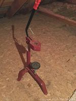 Photo of the red manual bottle corker showing lever, cork pressing plate, and tripod base on a wooden floor.