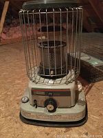 Full view of the portable heater with metal protective cage and base, set on a floor.