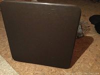 Photo showing a closed card table with a smooth dark brown surface and rounded edges, set upright on the floor.