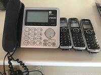 VTech phone system including base unit with answering system, three cordless handsets lined up, and coiled telephone cord.