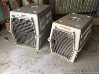 Two Pet Porter dog crates side by side on concrete floor inside storage area. Larger crate on left, medium crate on right. Beige plastic construction with metal doors and ventilation slots.