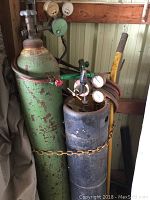 Front view showing two gas cylinders with attached regulators and hoses, torch handle, and yellow hand cart