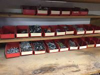 Photo showing two wooden shelves with 24 red plastic parts bins containing various screws, bolts, washers, nuts, and fasteners in different sizes and types.