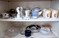 Shelves containing assorted servingware including silver items, porcelain candlestick holders, tea set, glass bowls, and plates.