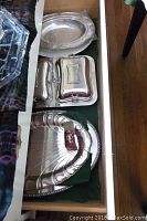 Drawer open to show various sterling silver serving plates, butter dishes, round plates, and a shell-shaped platter.