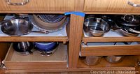 Two shelves of kitchen cabinetry holding various pots and pans including stainless steel and non-stick types, visible lids, and mixing bowls