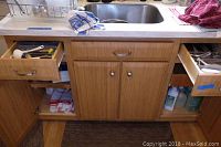 Photo of kitchen sink cabinet and drawers showing contents including kitchen utensils and cleaning supplies