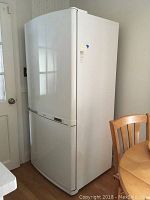 Full view of white Samsung refrigerator with bottom freezer compartment, showing door and overall shape.
