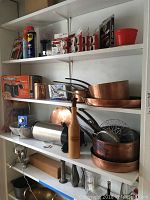 Overall view of white shelving unit holding copper cookware and assorted household items