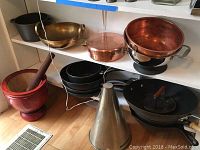 Top shelf showing cast iron pot, brass kadai and marble mortar with pestle