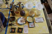 Top down view of multiple decorative tableware items on a yellow cloth including plates, bowls, trays, grinder, and small kitchen tools.