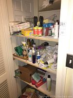 Three shelves inside a closet with a variety of cleaning and personal care supplies, including sprays, gloves, toothpaste, aerosol cans, and boxes