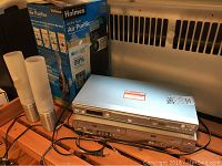 Photo shows Panasonic DVD player and Samsung DVD VHS player stacked horizontally with power cords visible. Also visible is a boxed Holmes HEPA-type Air Purifier behind the electronics.