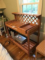Full view of the wood garden potting bench near a window, showing lattice back, slatted surfaces, and removable trays.