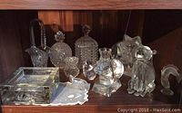 Front view showing all assorted Swarovski crystal pieces on wooden shelf, including decanter, baskets, bowls, and animal figurines.