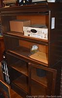 Front view of wooden shelf with two compartments, some items placed on shelves, glass paneled doors on bottom section