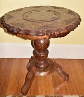 Side angle of wooden round accent table showing scalloped edge, pedestal base, and floral inlay detail.