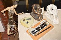 Photo showing two Vitruvian Collection figurines, the ceramic bird dish, and calligraphy set on a cloth-covered surface near a brick wall.