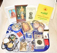 Tray holding an assortment of Thai keepsakes including coins, various amulets, bracelets, and four Thai religious/cultural booklets