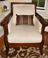 Front view of wood armchair with cream cushions and brown decorative pillow, showing wooden frame and curved armrests.
