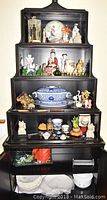 Full view of the black shelving unit displaying assorted figurines, large blue and white serving bowl, small decorative items, and IKEA white dishes below.