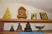 Shelf with six items including gold and wooden Buddha statues, glass case, and framed art.