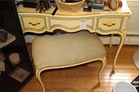 Front and side views of painted wood vanity table with three drawers showing chipping on paint surface and upholstered bench with beige cushion.