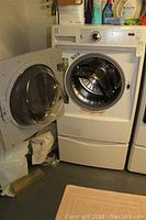 Front view of washer with door open showing interior drum and stacking pedestal