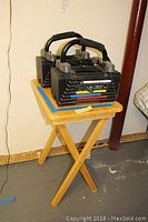 Overview of two adjustable dumbbells on small wood folding table against a wall.