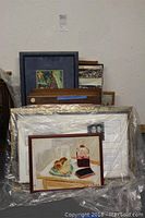 View of collection of framed art pieces stacked and wrapped in plastic.
