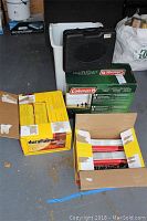 Image showing Duraflame fire logs in open boxes, Coleman cooking system box with black carrying case on top.