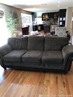 Front view of the brown fabric sofa placed on a hardwood floor with wooden armrests and base visible.