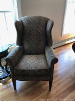Front view of the wingback chair showing the paisley upholstery and nailhead accents along the armrest.