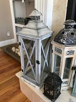 Large whitewashed wood and glass candle lantern with metal top, shown on shelf with other lanterns