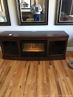 Front view of the electric fireplace cabinet placed on hardwood floor beneath large framed mirrors.