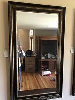 Framed rectangular wall mirror hanging on wall, reflective surface and frame detailed.