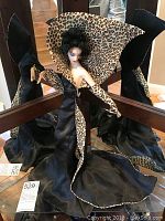 Front and side views of the 20 inch Erte style porcelain figurine wearing a black satin dress with leopard print lining and gloves, standing on a flat surface with mirrors showing multiple angles.