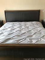 Front view of king size sleigh bed showing tufted bedspread, large wood frame, and leather inset headboard.