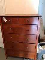 Front view of wooden chest of drawers showing five drawers and metal knobs, minor scratches visible.